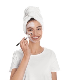 Happy young woman applying organic mask on her face against white background