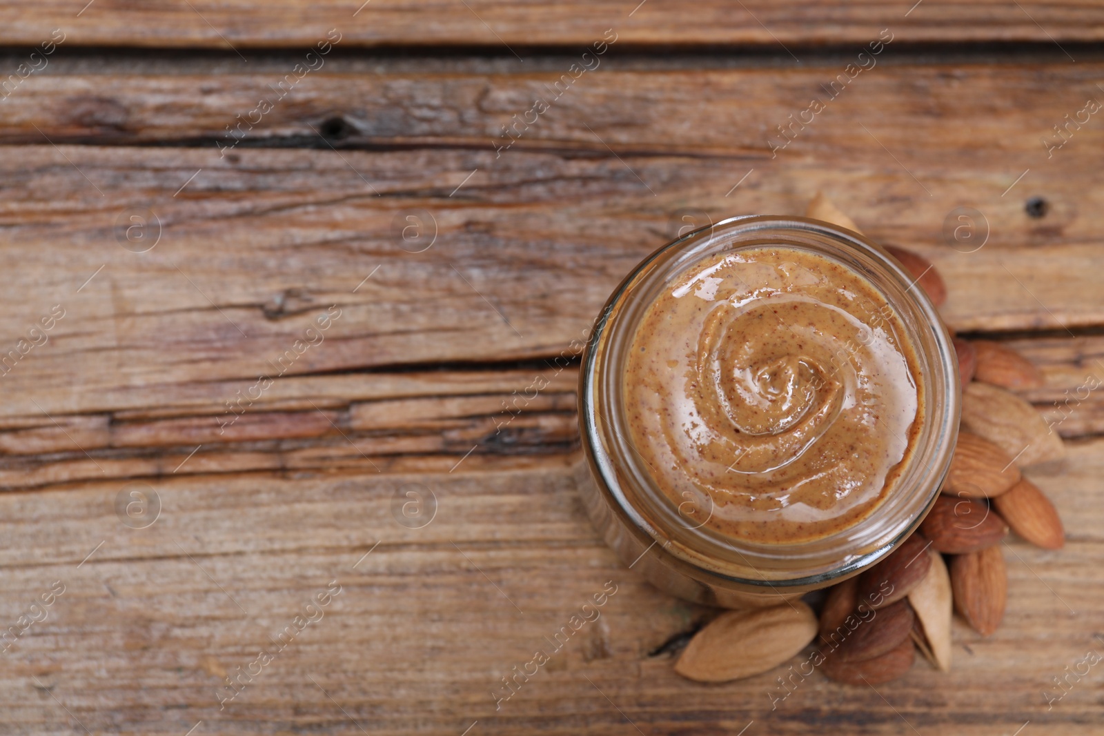 Photo of Tasty almond nut paste in jar on wooden table, top view. Space for text