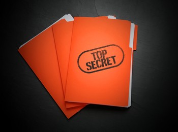 Image of Top Secret stamp. Orange files with documents on black table, top view
