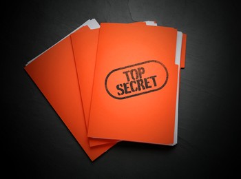 Top Secret stamp. Orange files with documents on black table, top view