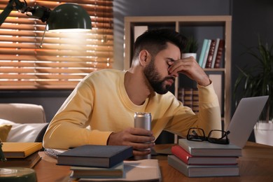 Tired young man with energy drink studying at home