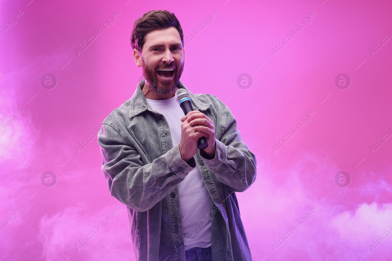 Photo of Handsome man with microphone singing on pink background