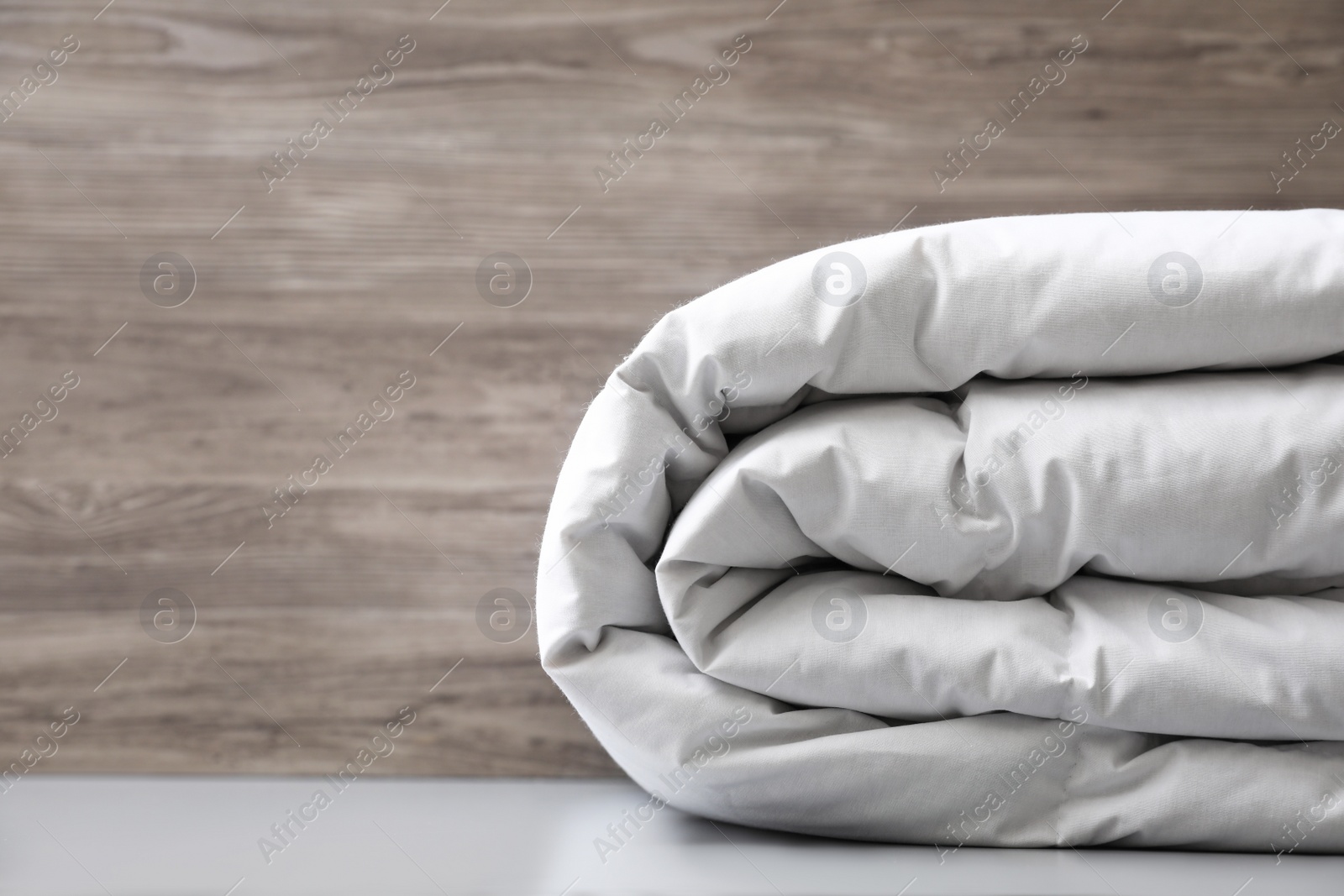 Photo of Soft folded blanket on light grey table, closeup. Space for text