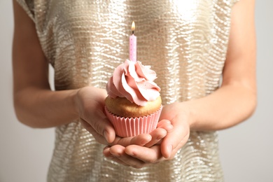 Photo of Woman holding delicious birthday cupcake with burning candle, closeup