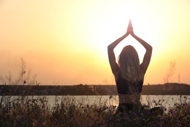 Photo of Young woman meditating near river at sunset, back view. Space for text