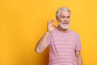 Photo of Senior man with mustache showing ok gesture on orange background, space for text