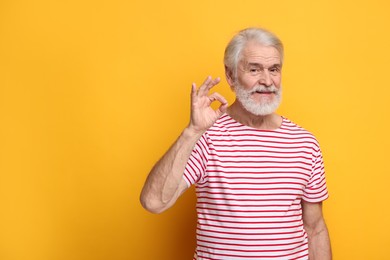 Senior man with mustache showing ok gesture on orange background, space for text