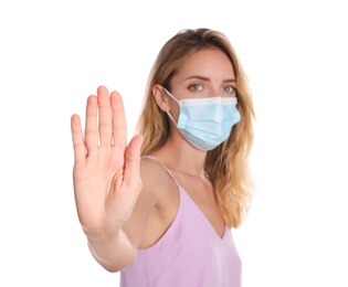Photo of Woman in protective face mask showing stop gesture on white background, focus on hand. Prevent spreading of coronavirus