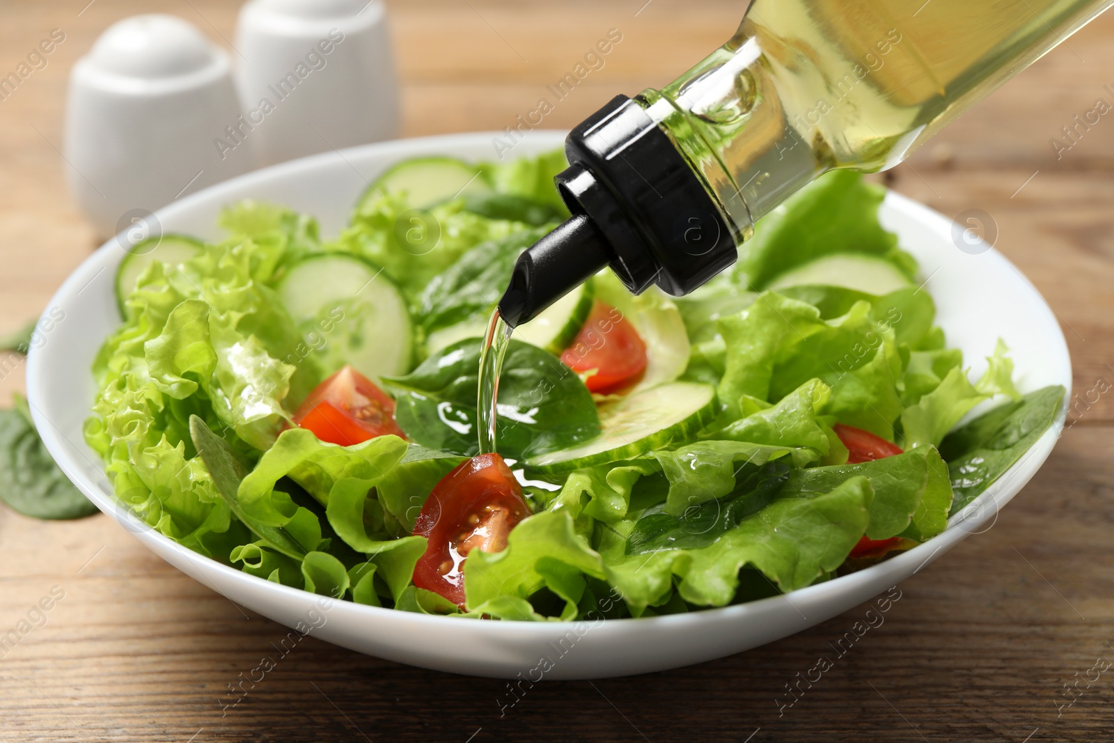 Photo of Pouring oil into tasty salad on table, closeup