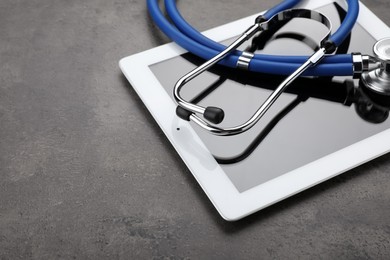 Photo of Computer tablet with stethoscope on grey table, closeup. Space for text