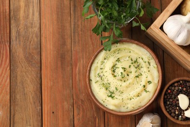 Photo of Bowl of tasty mashed potato, parsley, garlic and pepper on wooden table, flat lay, Space for text
