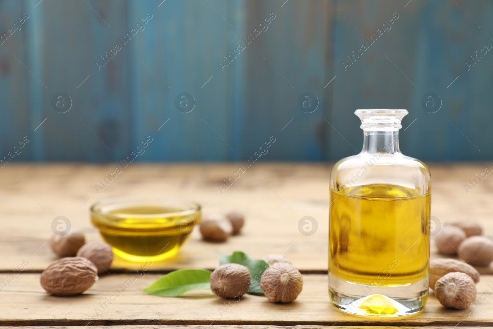 Photo of Bottle of nutmeg oil, nuts on wooden table, space for text