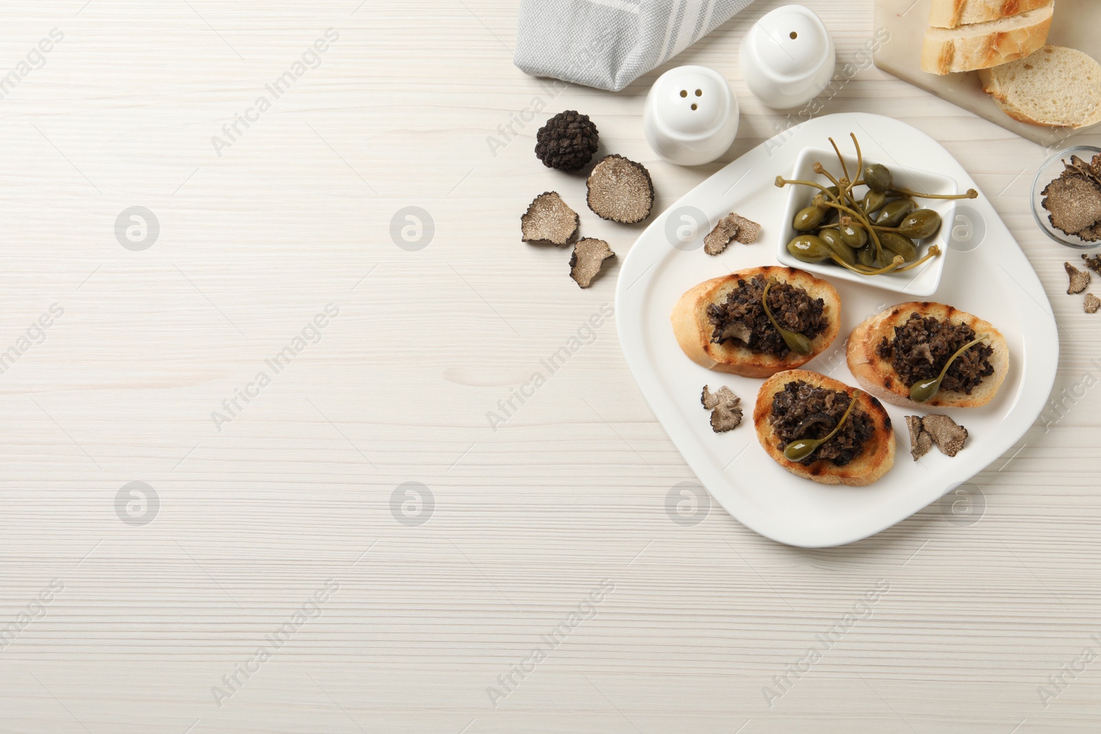 Photo of Delicious bruschettas with truffle sauce and caperberries on white wooden table, flat lay. Space for text