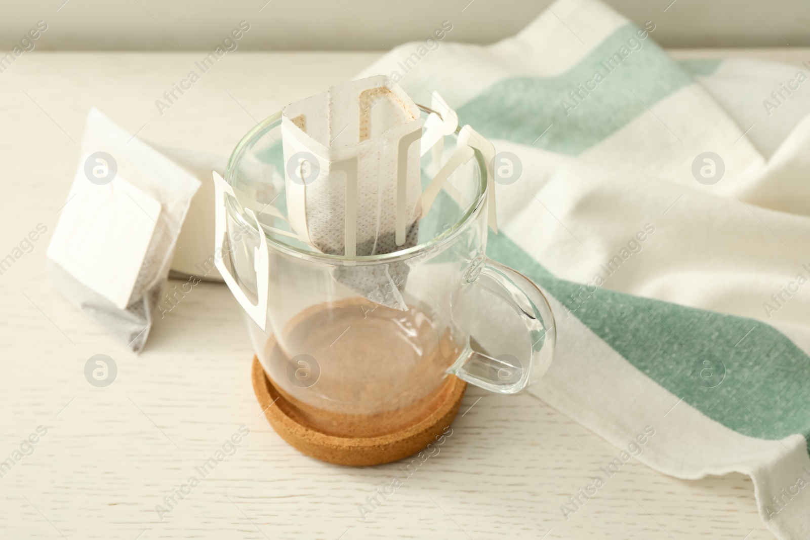 Photo of Drip coffee bags and glass cup on white wooden table, closeup