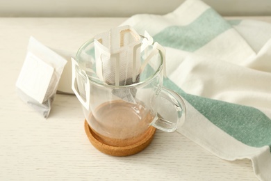Photo of Drip coffee bags and glass cup on white wooden table, closeup
