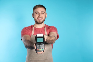 Young seller holding payment terminal on color background. Space for text