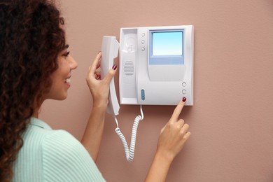Photo of Young African-American woman pressing button on intercom panel indoors