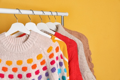 Collection of warm sweaters hanging on rack against color background. Space for text