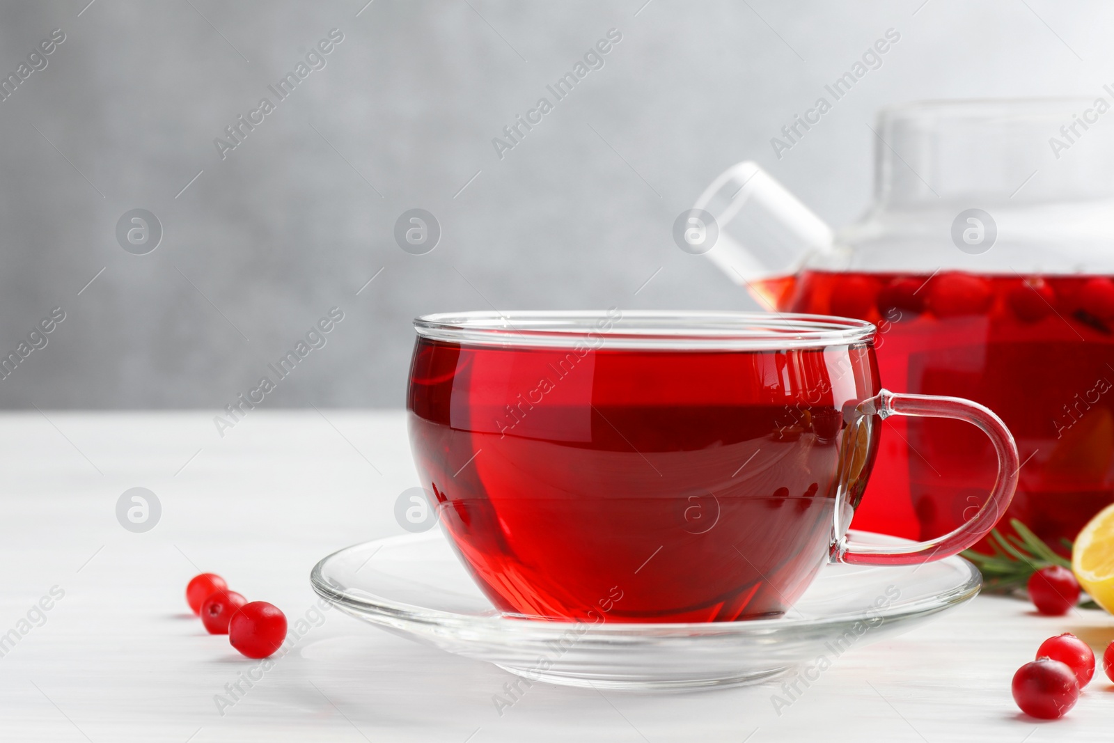 Photo of Tasty hot cranberry tea in glass cup and fresh berries on white table