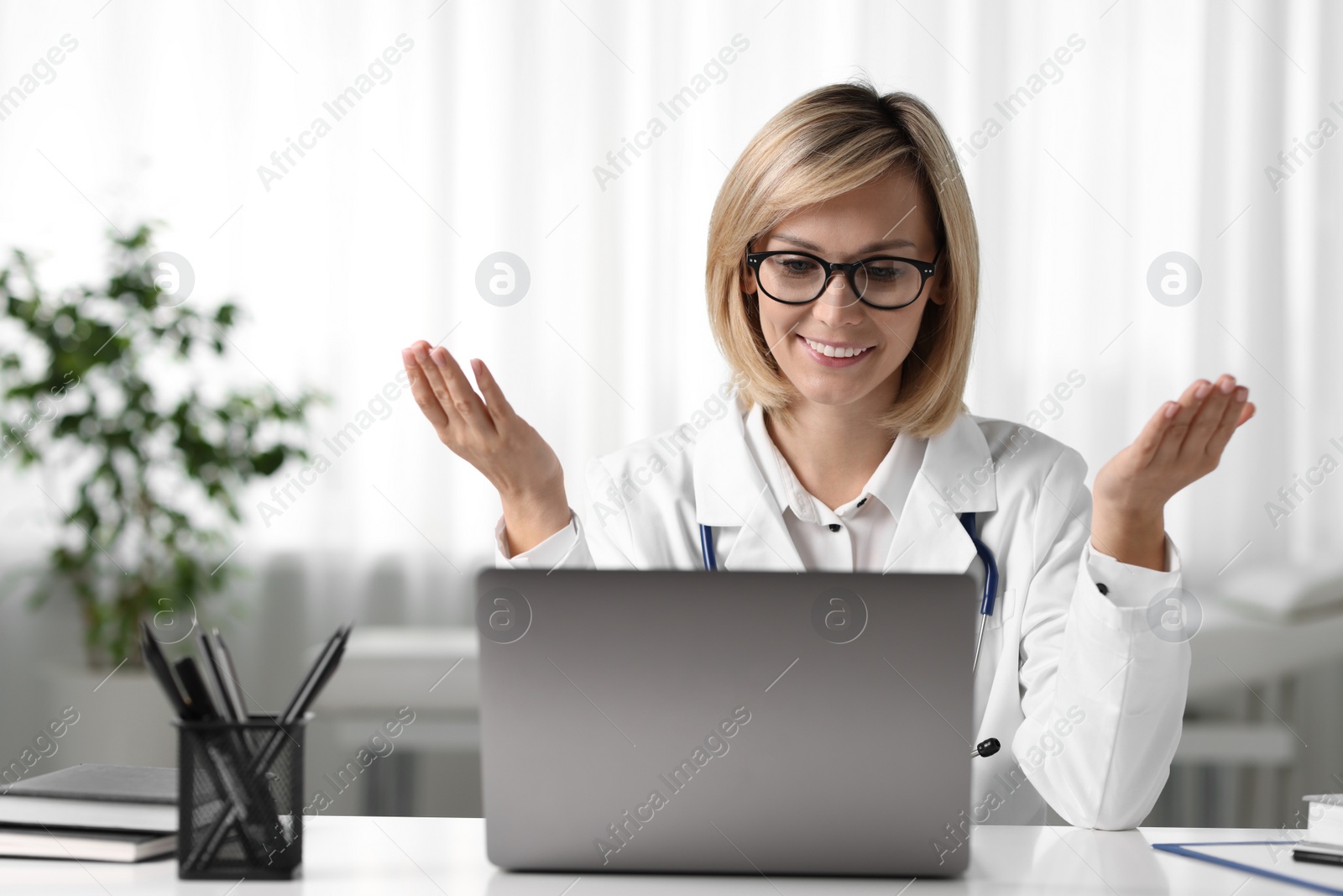 Photo of Smiling doctor with laptop having online consultation at table in office