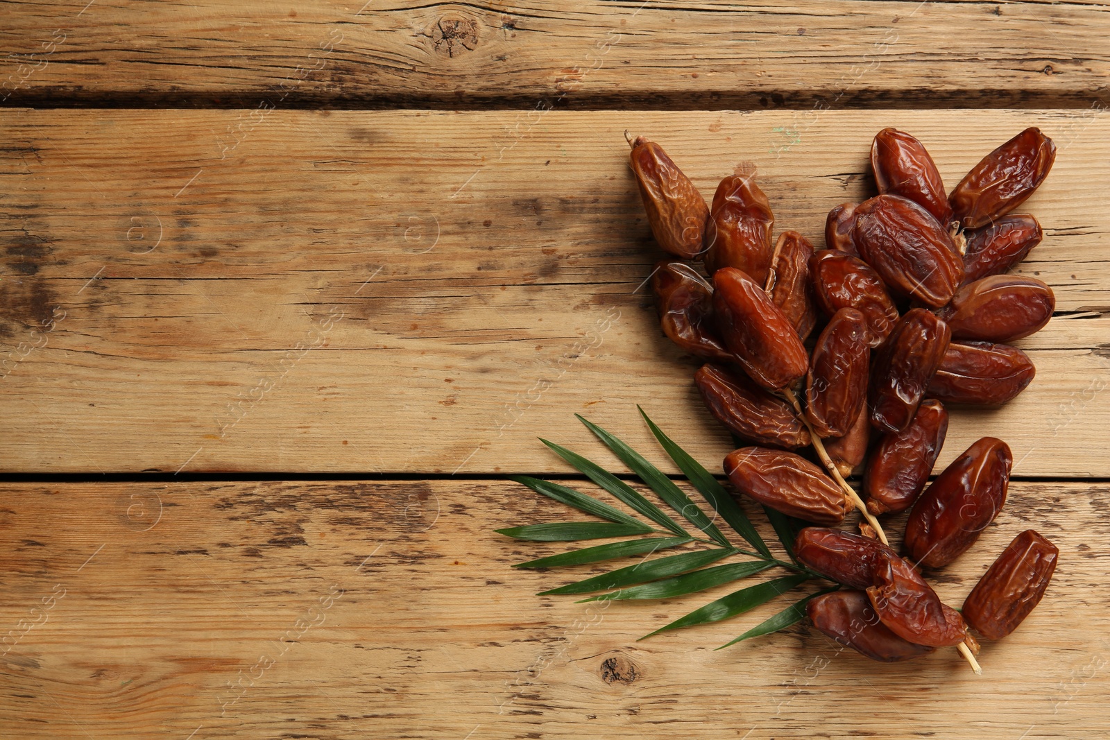 Photo of Sweet dried dates with green leaf on wooden table, flat lay. Space for text