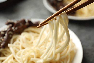 Photo of Chopsticks with tasty cooked rice noodles over plate, closeup