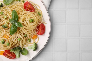 Photo of Delicious pasta primavera with tomatoes, basil and broccoli on white tiled table, top view. Space for text