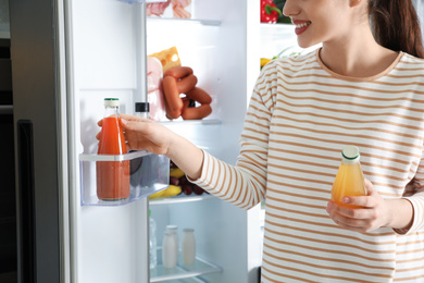 Photo of Young woman taking juice out of refrigerator indoors, closeup