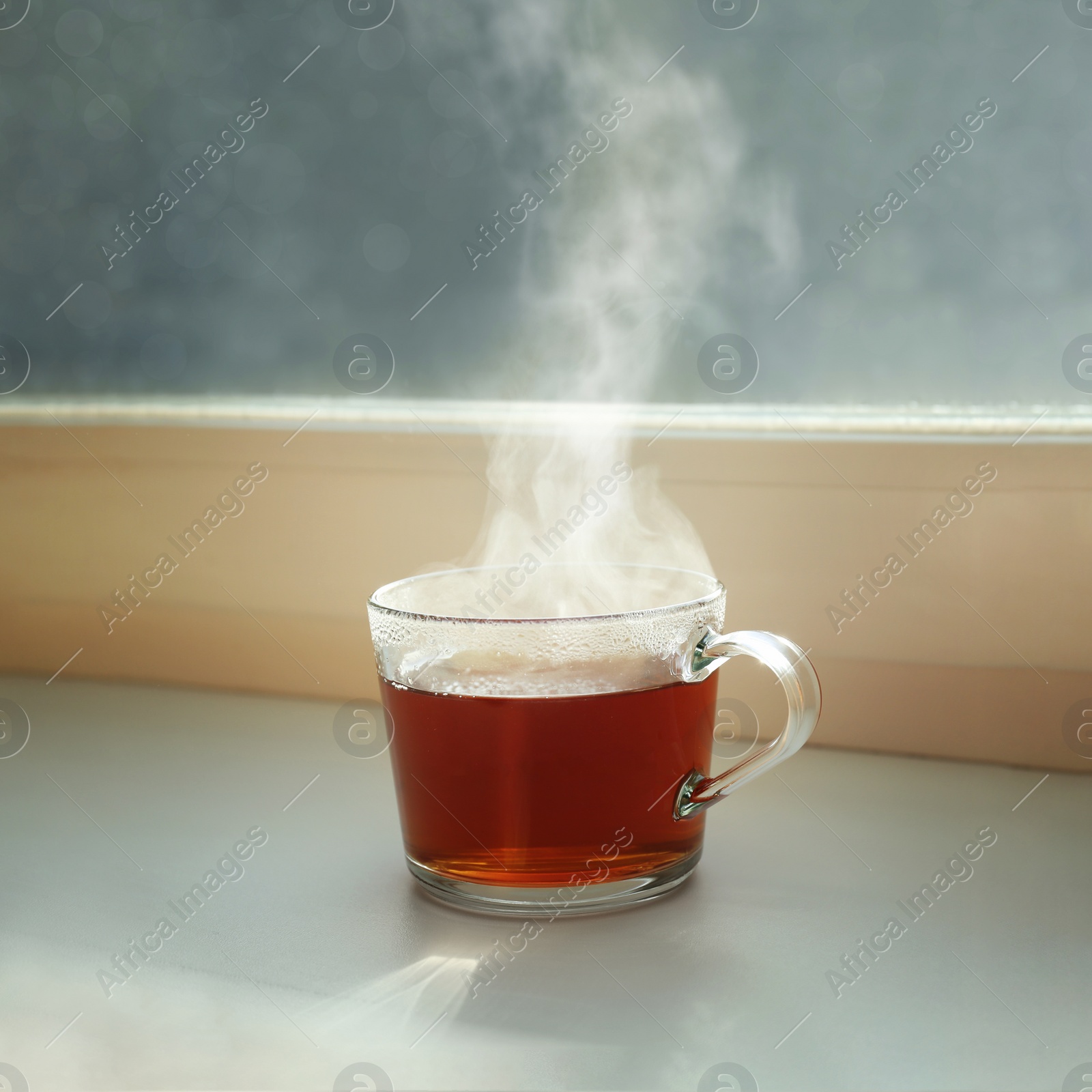 Photo of Cup of hot tea near window on rainy day