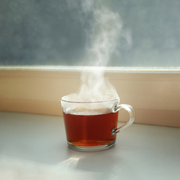 Photo of Cup of hot tea near window on rainy day