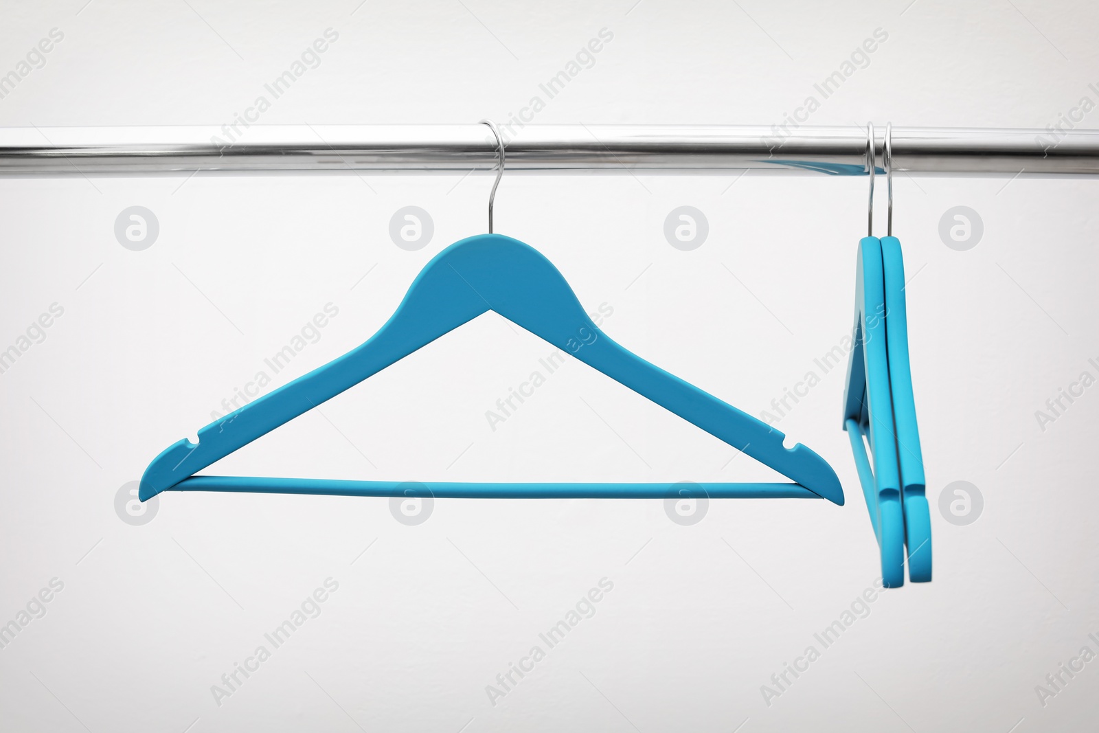 Photo of Clothes hangers on metal rail against light background