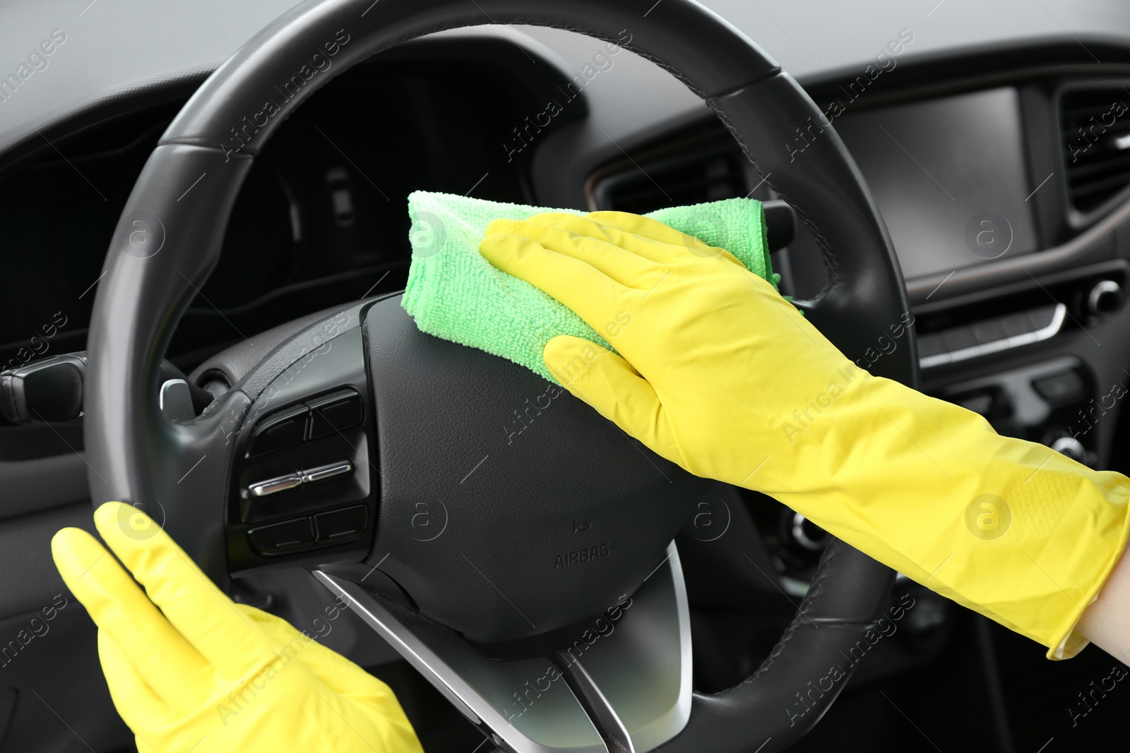 Photo of Woman cleaning steering wheel with rag in car, closeup