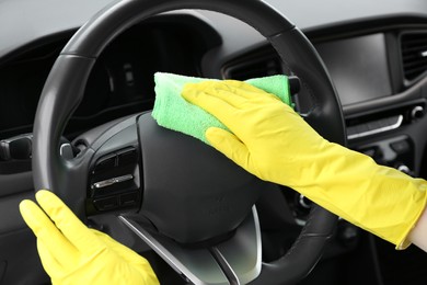 Photo of Woman cleaning steering wheel with rag in car, closeup