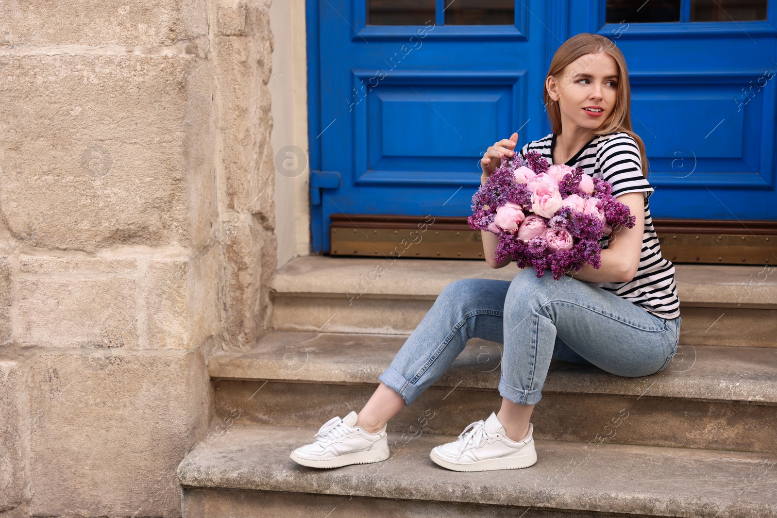 Photo of Beautiful woman with bouquet of spring flowers on stairs near building, space for text