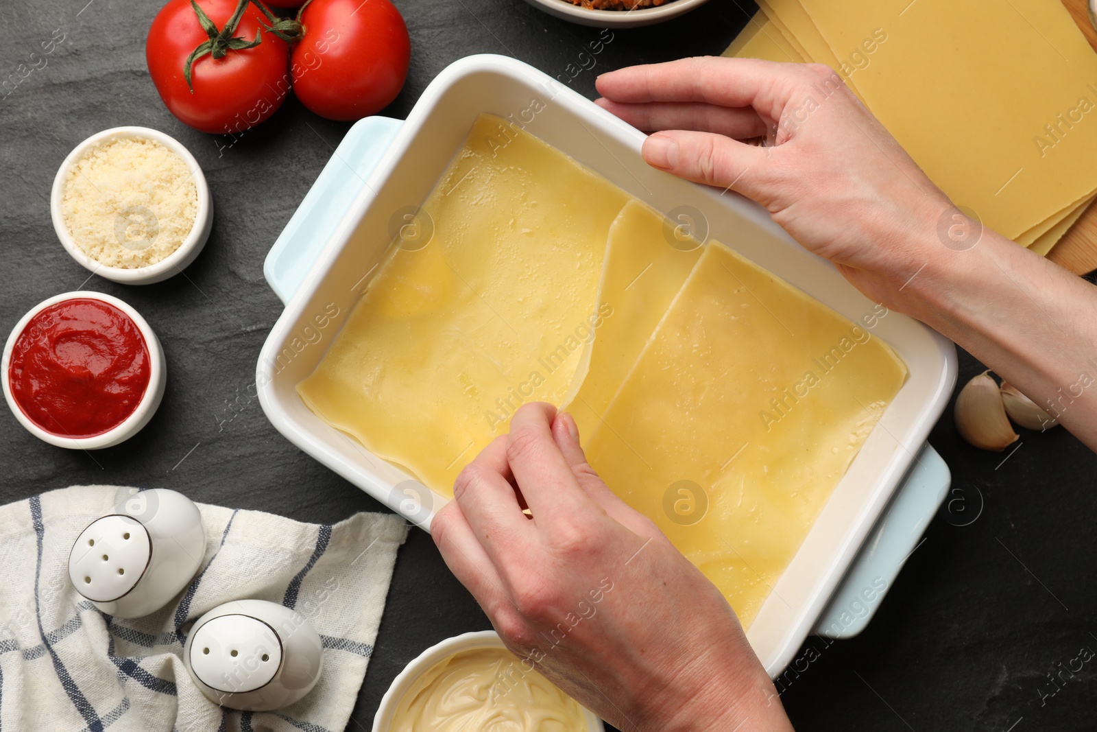 Photo of Woman making lasagna at dark table, top view