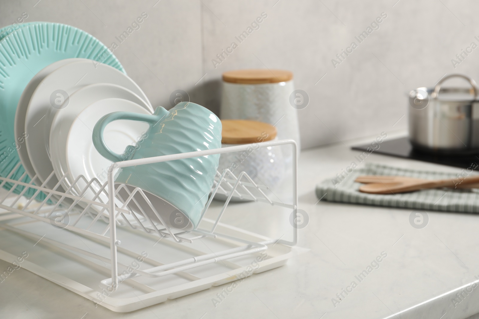 Photo of Drainer with different clean dishware and cup on light table indoors