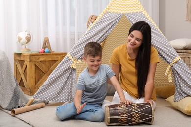 Photo of Mother and son playing on drum near toy wigwam at home