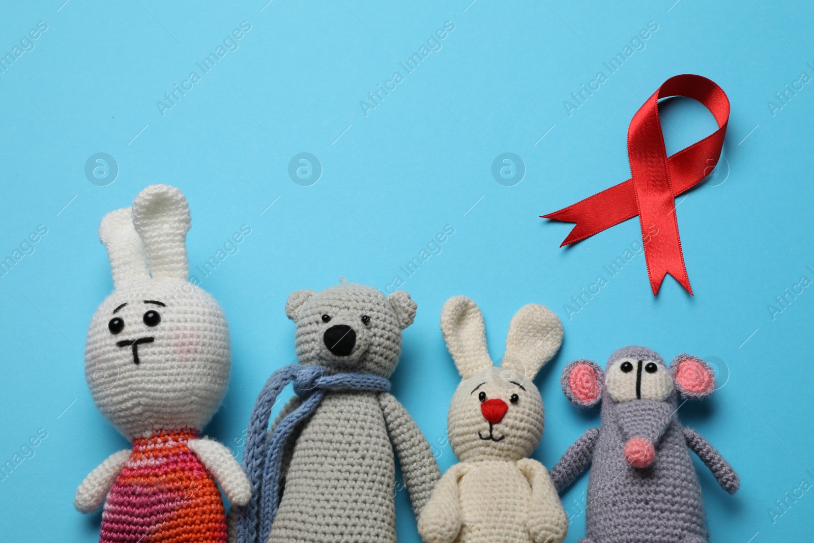 Photo of Cute knitted toys and red ribbon on blue background, flat lay. AIDS disease awareness