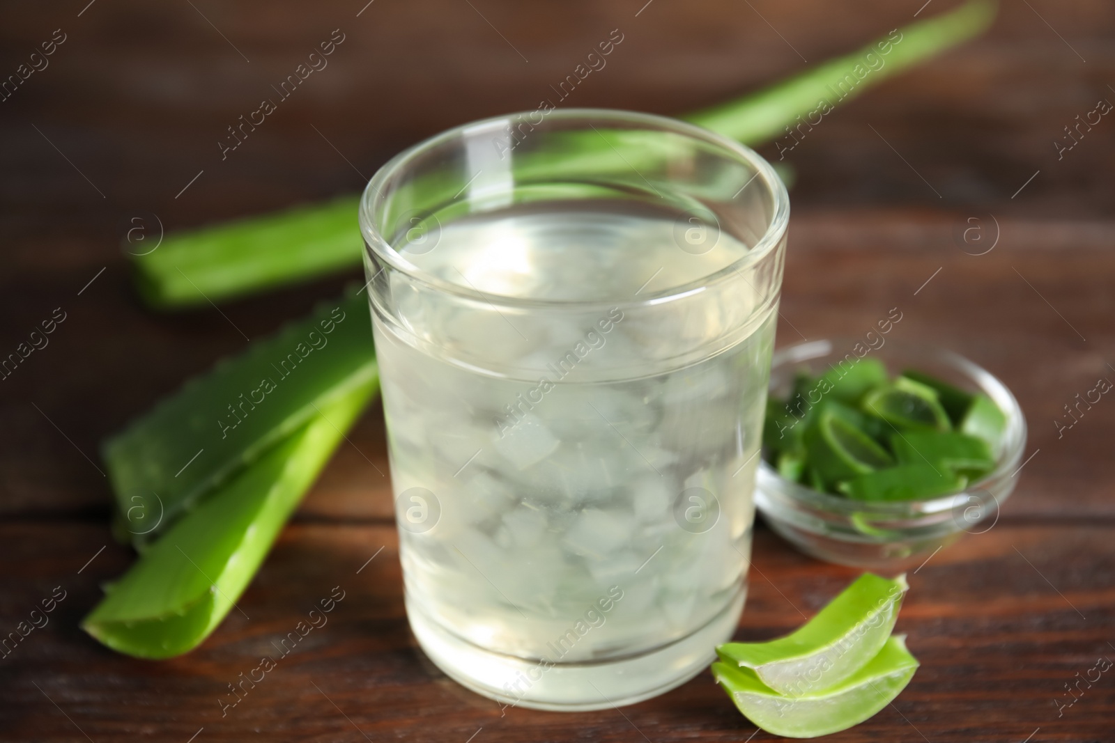 Photo of Fresh aloe drink in glass and leaves on wooden table