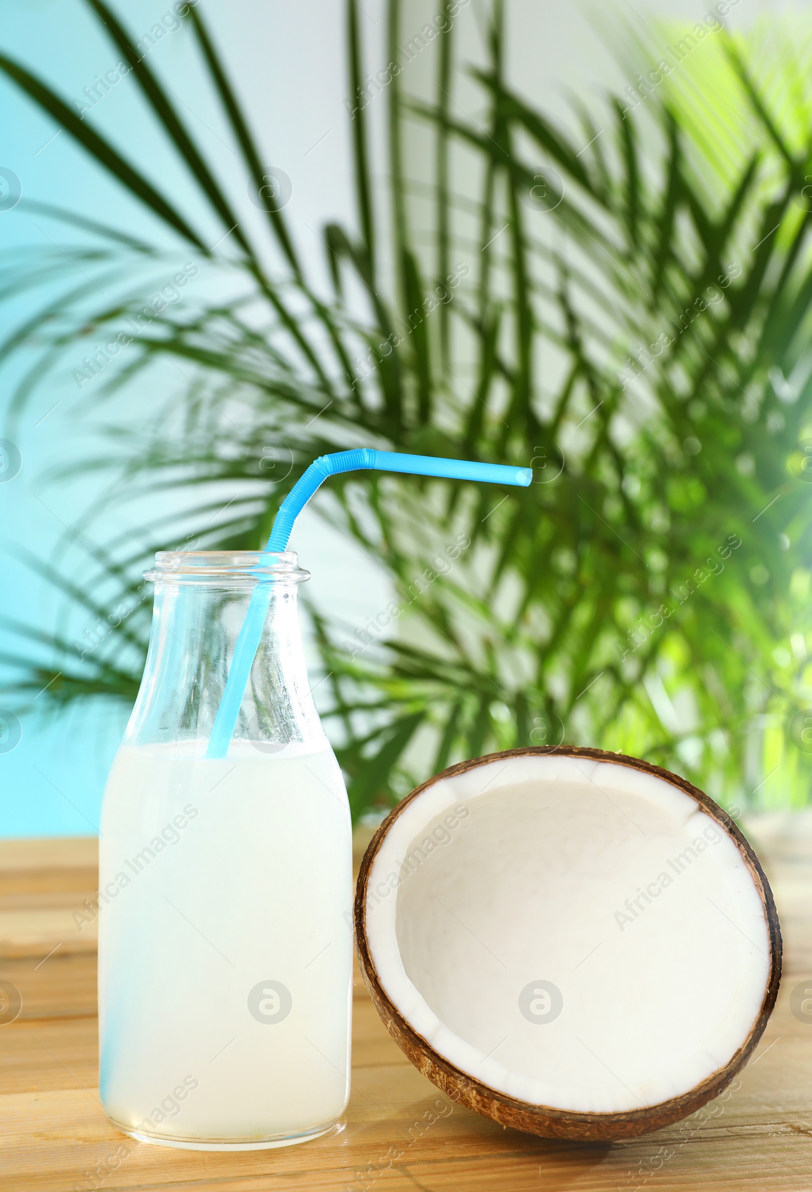 Photo of Composition with bottle of coconut water on wooden table against blue background