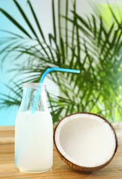 Composition with bottle of coconut water on wooden table against blue background