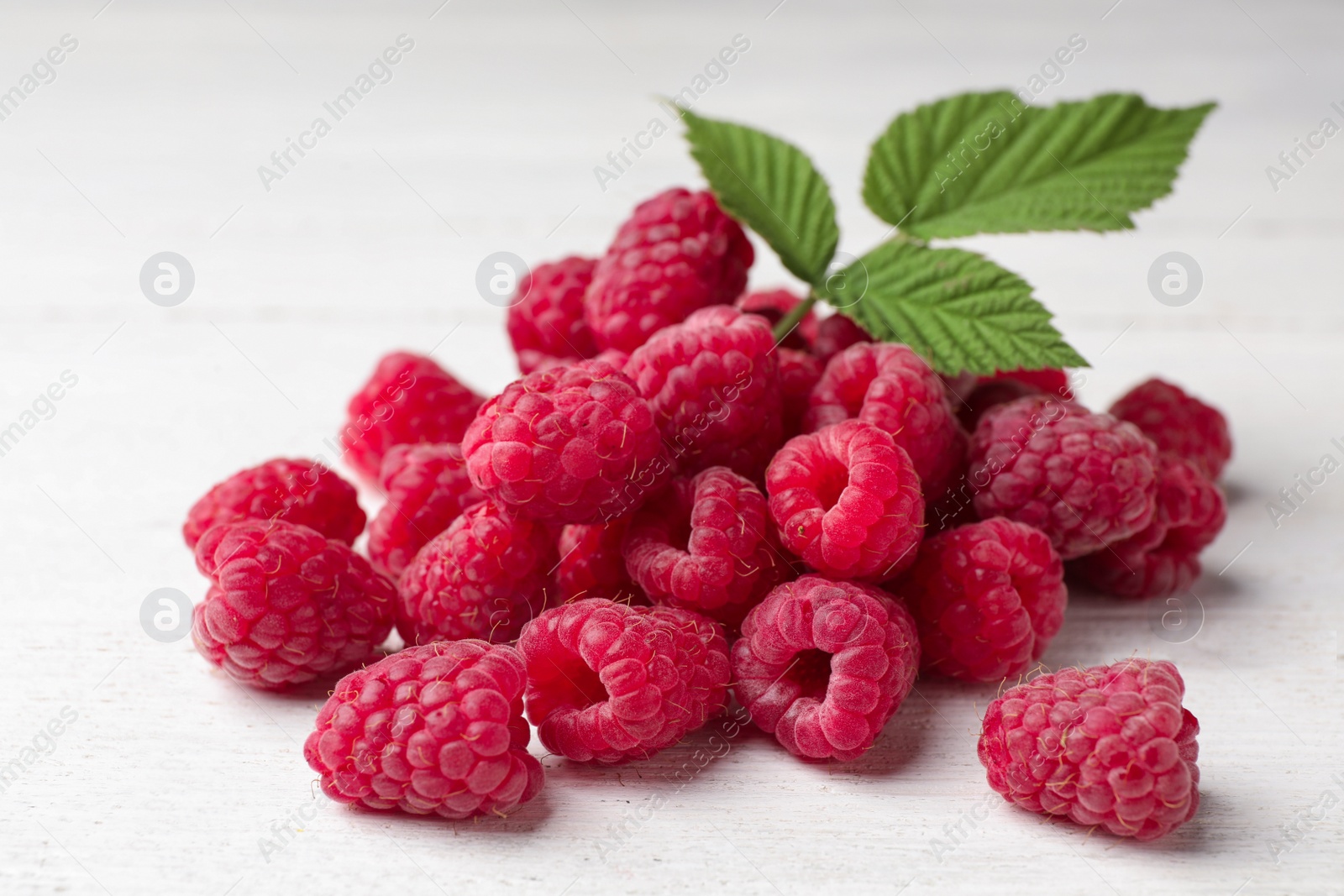 Photo of Delicious fresh ripe raspberries with leaves on white wooden table, closeup view