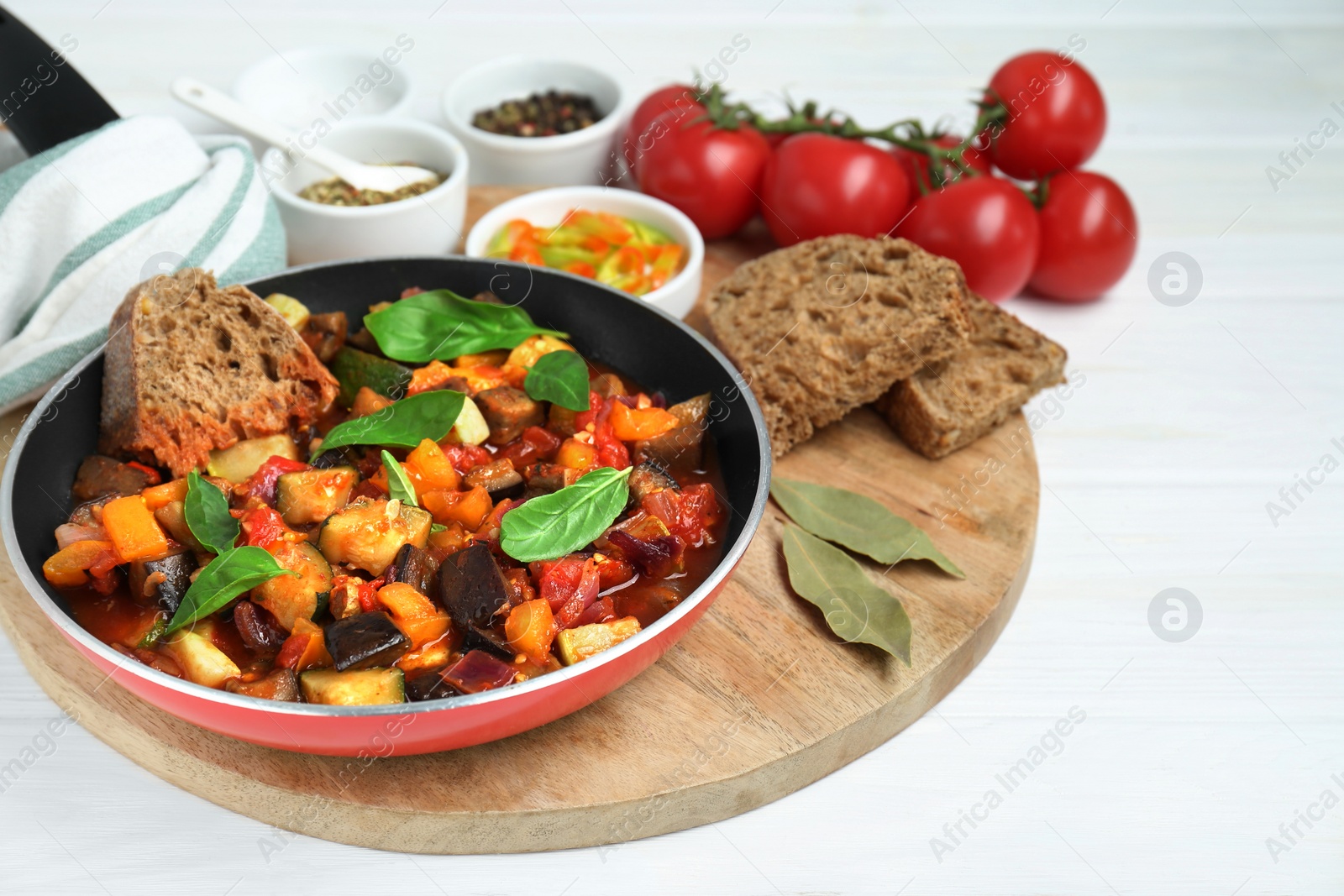Photo of Dish with tasty ratatouille, bread and basil on white wooden table
