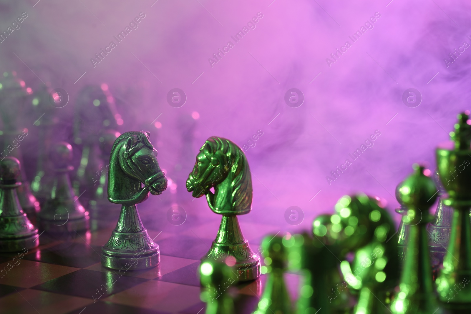 Photo of Two knights and other chess pieces on checkerboard in color light, selective focus. Space for text