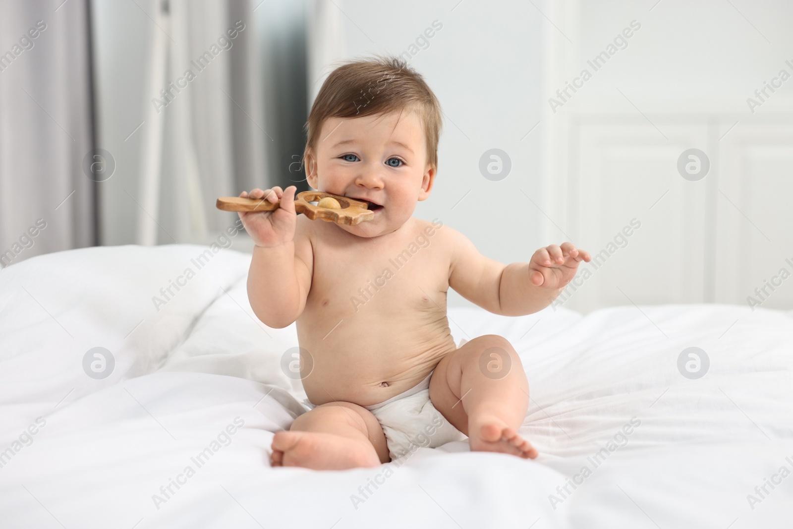 Photo of Cute baby boy with wooden rattle on bed at home