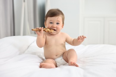 Photo of Cute baby boy with wooden rattle on bed at home