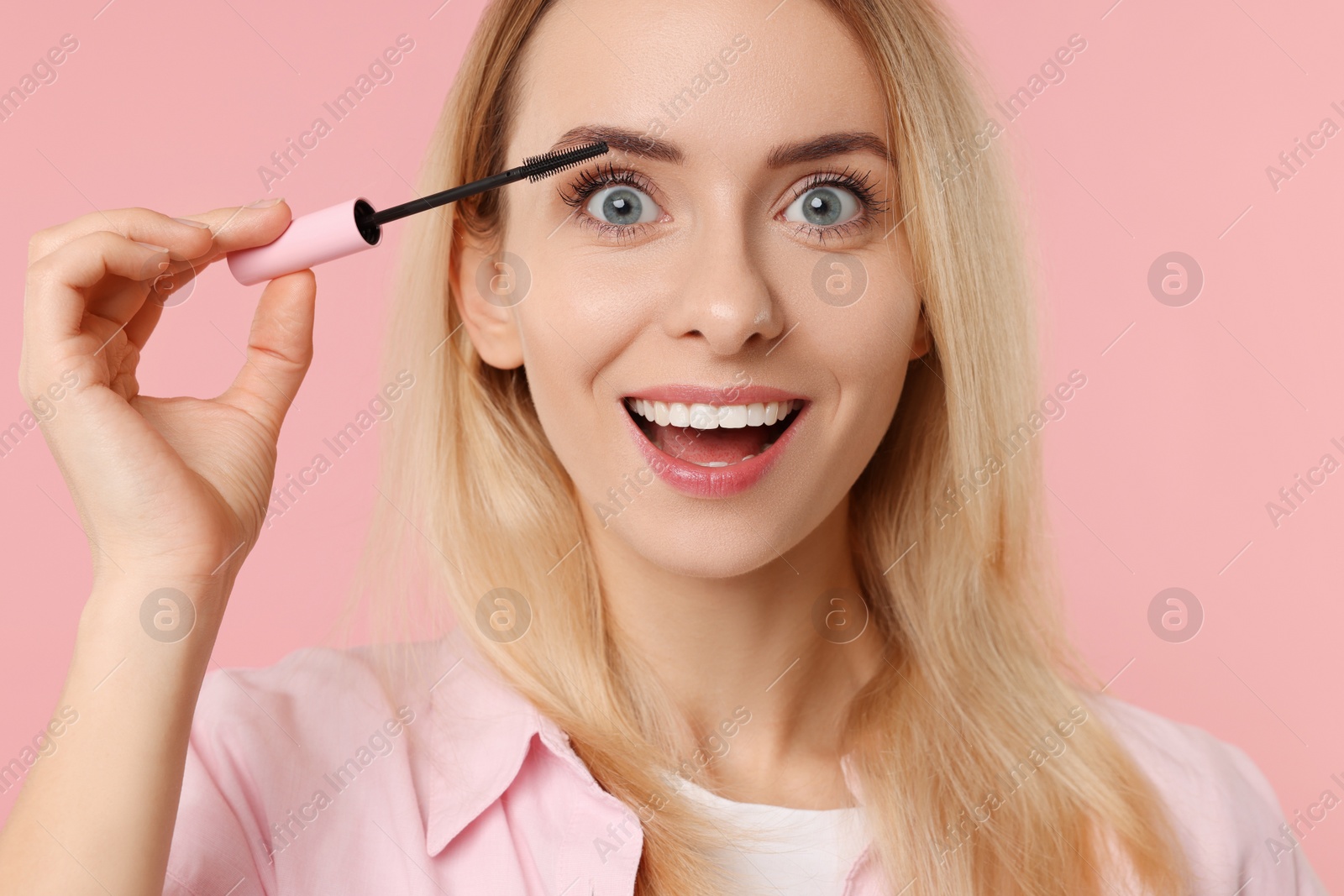 Photo of Beautiful woman applying mascara on pink background, closeup