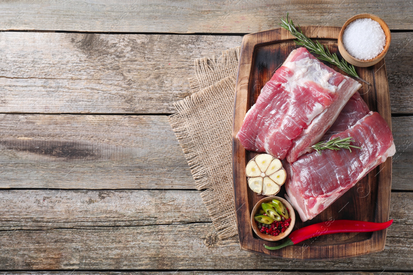 Photo of Pieces of raw pork belly, garlic, salt and spices on wooden table, top view. Space for text