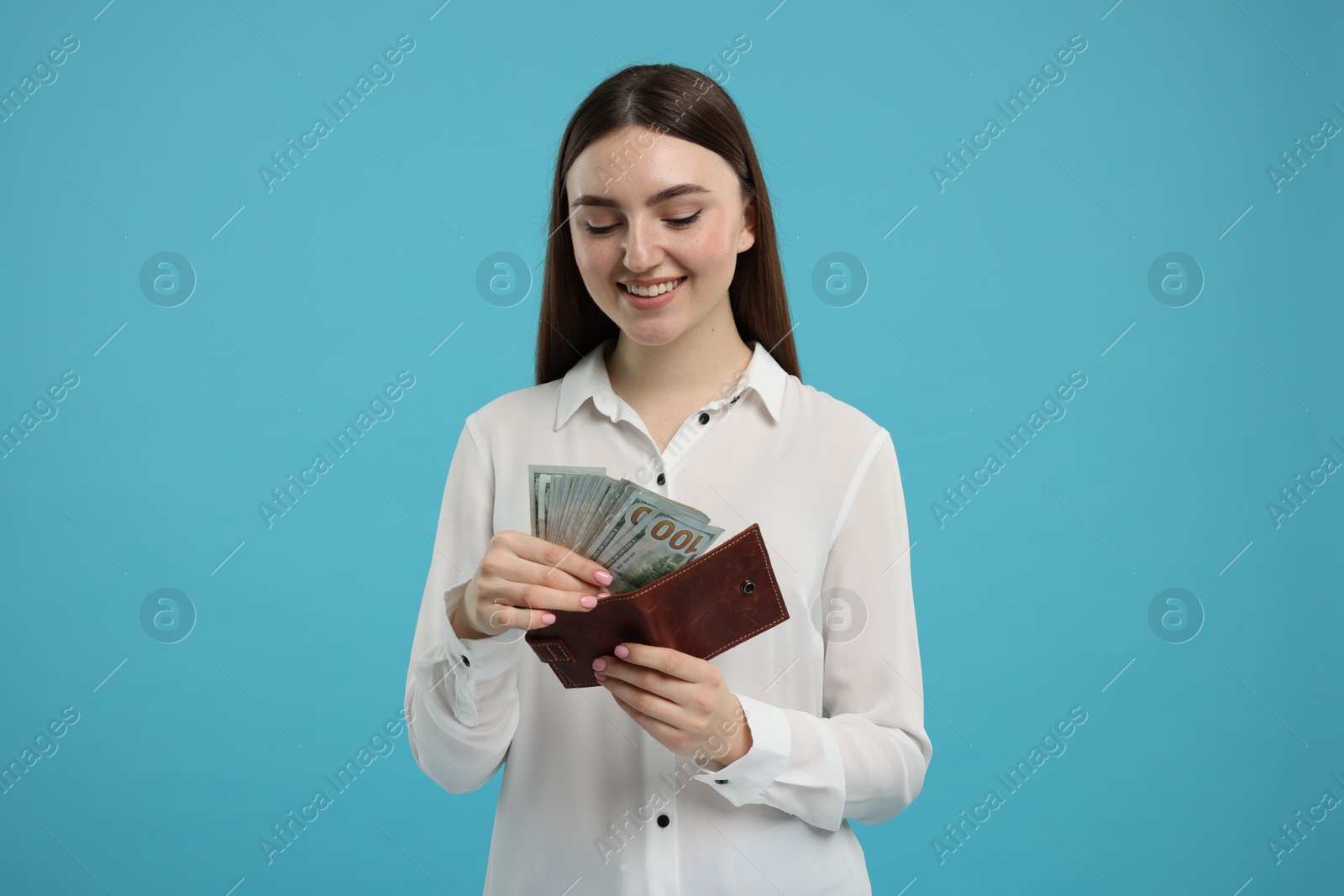 Photo of Happy woman putting money into wallet on light blue background