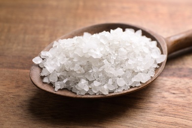 Photo of Spoon with white sea salt on wooden table, closeup. Spa treatment